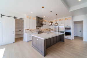 Kitchen with white cabinets, hanging light fixtures, a barn door, a kitchen island with sink, and appliances with stainless steel finishes