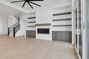 Unfurnished living room with stairway, light wood-type flooring, a ceiling fan, a glass covered fireplace, and recessed lighting