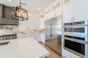 Kitchen featuring stainless steel appliances, white cabinetry, tasteful backsplash, hanging light fixtures, and light wood-type flooring