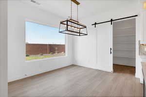 Unfurnished dining area with wood finished floors, plenty of natural light, a barn door, and a chandelier