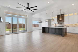 Kitchen featuring light countertops, a chandelier, open floor plan, a ceiling fan, and an island with sink