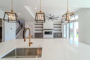 Kitchen with pendant lighting, ceiling fan with notable chandelier, sink, and light stone counters