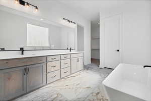 Full bathroom with marble tiled floors, double vanity, and a freestanding tub