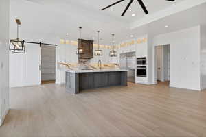 Kitchen with appliances with stainless steel finishes, light countertops, a barn door, a spacious island, and white cabinetry