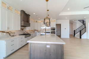 Kitchen with light wood-type flooring, backsplash, appliances with stainless steel finishes, a large island with sink, and white cabinets