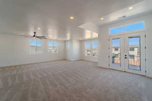 Unfurnished living room featuring a textured ceiling, french doors, light colored carpet, and ceiling fan