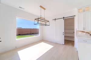 Unfurnished dining area with an inviting chandelier, light wood-type flooring, and a barn door