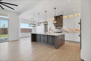 Kitchen featuring light countertops, decorative backsplash, a kitchen island with sink, white cabinets, and light wood finished floors