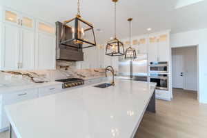 Kitchen featuring stainless steel appliances, sink, hanging light fixtures, white cabinets, and a large island