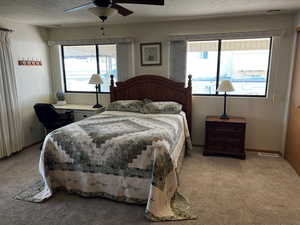 Carpeted bedroom with a textured ceiling, multiple windows, and ceiling fan