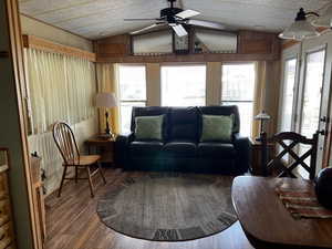 Living room with a wealth of natural light, wooden walls, wood-type flooring, and vaulted ceiling