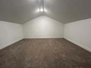 Additional living space with dark colored carpet, lofted ceiling, and a textured ceiling