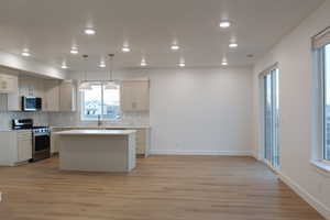 Kitchen with a kitchen island, light wood-type flooring, appliances with stainless steel finishes, and pendant lighting