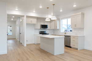 Kitchen with a center island, hanging light fixtures, tasteful backsplash, light wood-type flooring, and appliances with stainless steel finishes