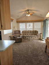 Living room with ceiling fan, dark carpet, lofted ceiling, and a textured ceiling