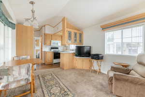 Kitchen featuring open floor plan, lofted ceiling, white appliances, light brown cabinetry, and glass insert cabinets