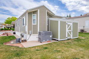 Back of house with an outbuilding, a patio, a storage unit, central AC, and a lawn