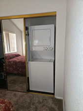 Clothes washing area featuring stacked washer and dryer and carpet