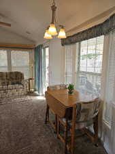 Carpeted dining area featuring lofted ceiling, a wealth of natural light, and a chandelier