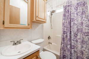 Bathroom featuring shower / bathtub combination with curtain, wallpapered walls, toilet, and vanity