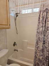 Bathroom with shower / bath combination with curtain and toilet