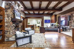 Living room featuring hardwood / wood-style flooring, beam ceiling, and a stone fireplace