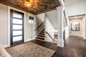 Foyer entrance with dark hardwood / wood-style flooring, ornate columns, and wood ceiling