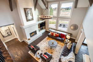 Living room with dark hardwood / wood-style floors, a towering ceiling, a fireplace, beamed ceiling, and a notable chandelier