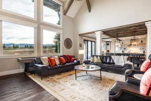 Living room with ornate columns, an inviting chandelier, dark hardwood / wood-style flooring, high vaulted ceiling, and beamed ceiling