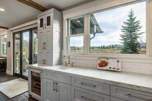 Kitchen featuring sink, dark wood-type flooring, beverage cooler, tasteful backsplash, and light stone counters