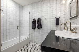 Bathroom featuring sink, enclosed tub / shower combo, and tile walls