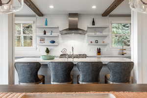 Kitchen with beamed ceiling, a kitchen breakfast bar, tasteful backsplash, and wall chimney range hood