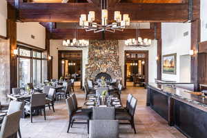 Tiled dining room featuring beam ceiling, a stone fireplace, and a high ceiling