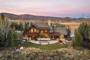 Back house at dusk featuring a mountain view, a yard, a patio, and a hot tub