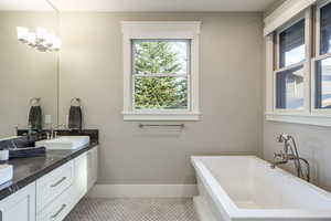 Bathroom with a chandelier, vanity, a tub to relax in, and tile patterned floors