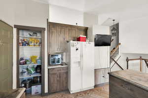 Kitchen with white refrigerator with ice dispenser, pendant lighting, light hardwood / wood-style floors, and dark brown cabinets