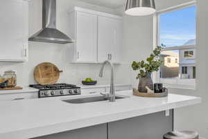 Kitchen featuring white cabinets, wall chimney exhaust hood, sink, and stainless steel range