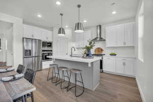 Kitchen featuring white cabinets, sink, stainless steel appliances, and wall chimney range hood