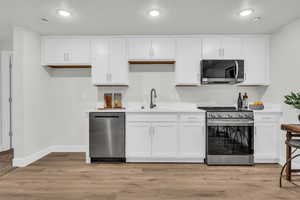 Kitchen with sink, light wood-type flooring, a textured ceiling, appliances with stainless steel finishes, and white cabinetry