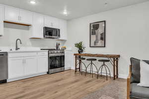 Kitchen featuring light hardwood / wood-style floors, white cabinetry, sink, and appliances with stainless steel finishes