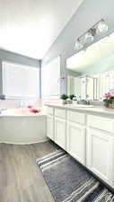 Bathroom featuring vanity, a textured ceiling, shower with separate bathtub, hardwood / wood-style floors, and lofted ceiling