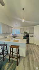 Kitchen featuring kitchen peninsula, decorative light fixtures, black range with electric stovetop, and lofted ceiling