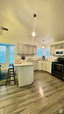 Kitchen featuring sink, hanging light fixtures, black / electric stove, light hardwood / wood-style floors, and a breakfast bar area