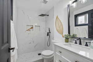 Bathroom featuring tiled shower, vanity, and toilet