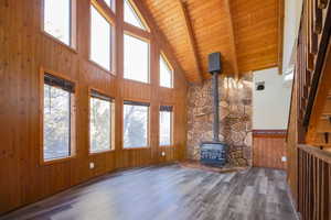 Unfurnished living room with hardwood / wood-style floors, a wood stove, high vaulted ceiling, wooden ceiling, and beam ceiling