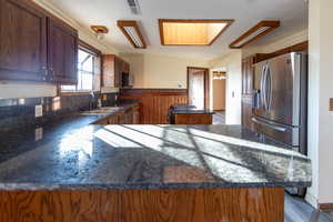 Kitchen with dark stone countertops, light hardwood / wood-style floors, kitchen peninsula, sink, and stainless steel appliances