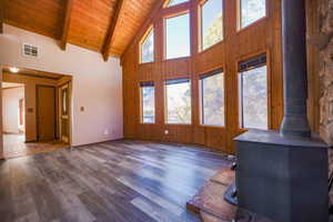 Unfurnished living room with dark hardwood / wood-style flooring, beamed ceiling, a wood stove, high vaulted ceiling, and wooden ceiling