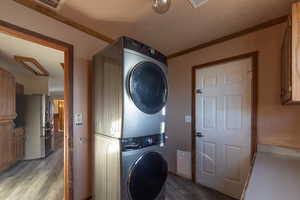 Clothes washing area featuring stacked washing maching and dryer, ornamental molding, a textured ceiling, and hardwood / wood-style floors