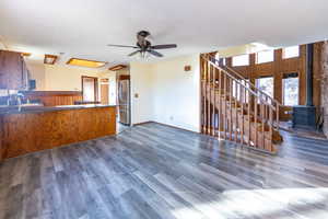 Kitchen with ceiling fan, kitchen peninsula, dark wood-type flooring, a wood stove, and stainless steel fridge