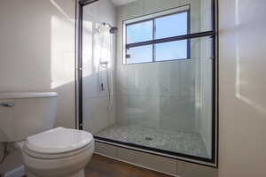 Bathroom with toilet, a shower with shower door, and wood-type flooring